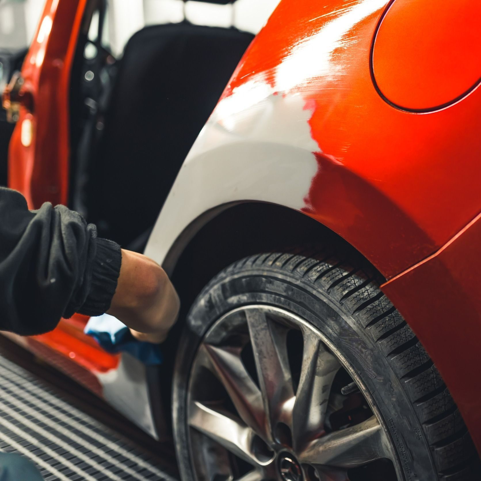 Una persona está pintando el costado de un auto rojo.