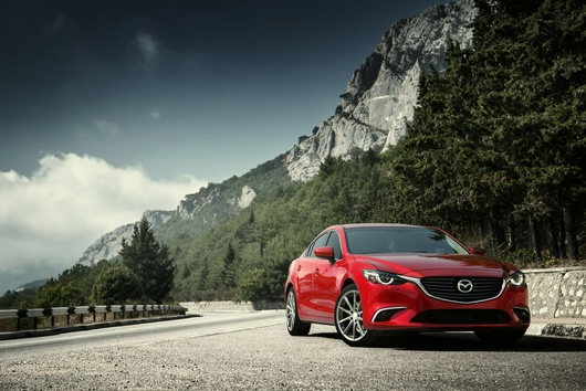 Un Mazda 6 rojo está estacionado al costado de una carretera de montaña.