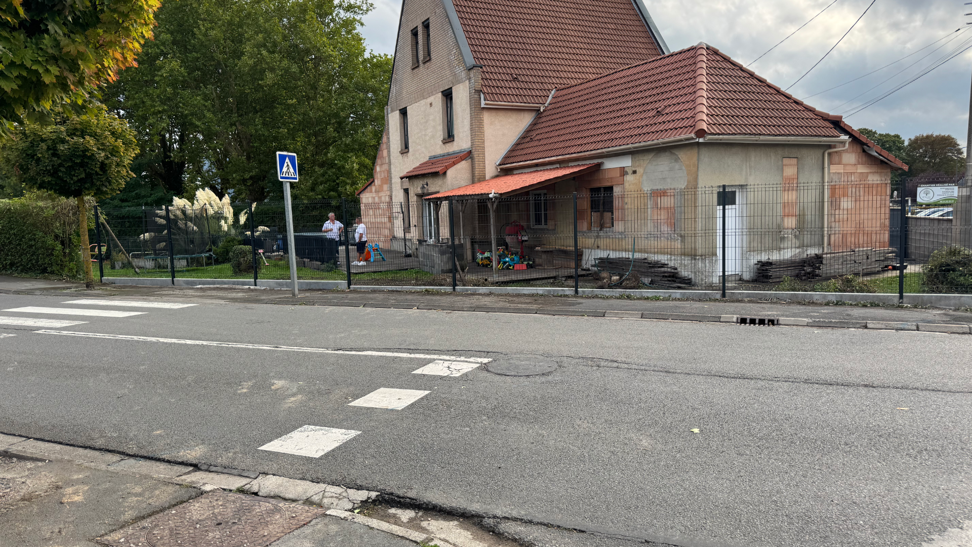 Vue de la rue d'un bâtiment au toit rouge, de personnes debout sur le porche.