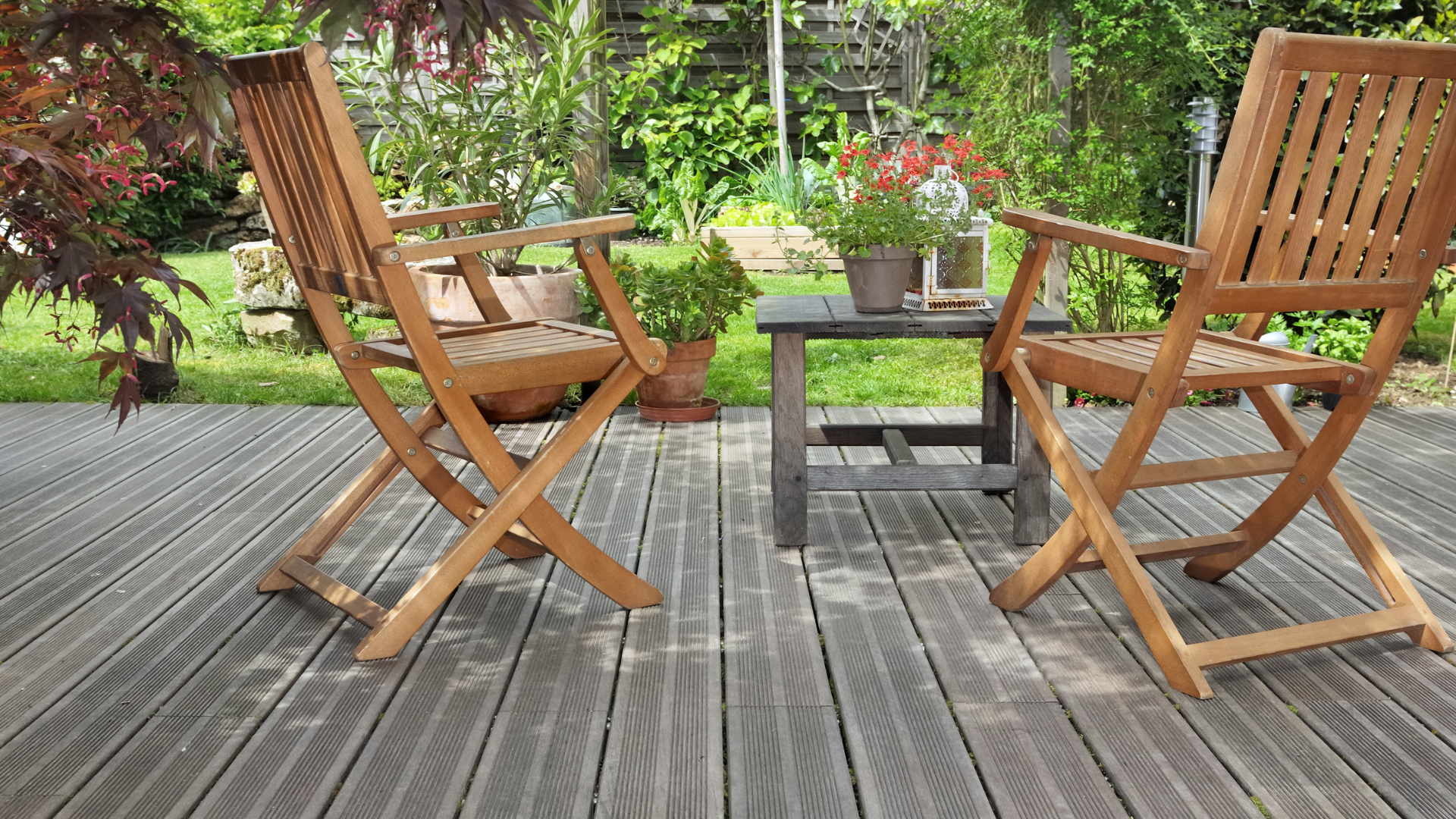 Chaises en bois et petite table sur une terrasse, donnant sur un jardin.