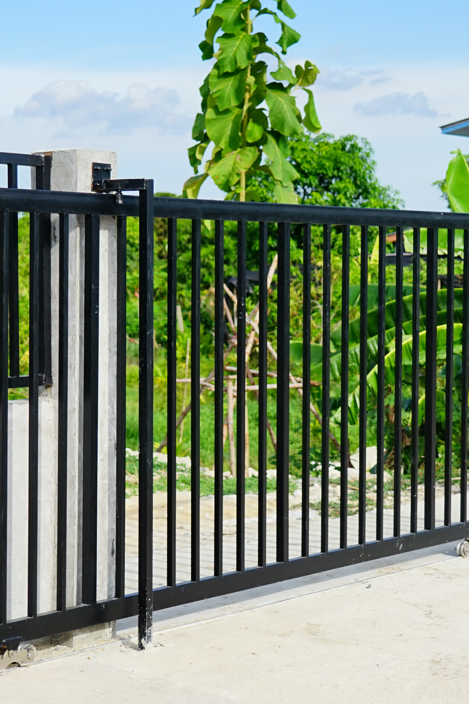 Clôture métallique noire à barreaux verticaux. Feuillage vert visible derrière la clôture.
