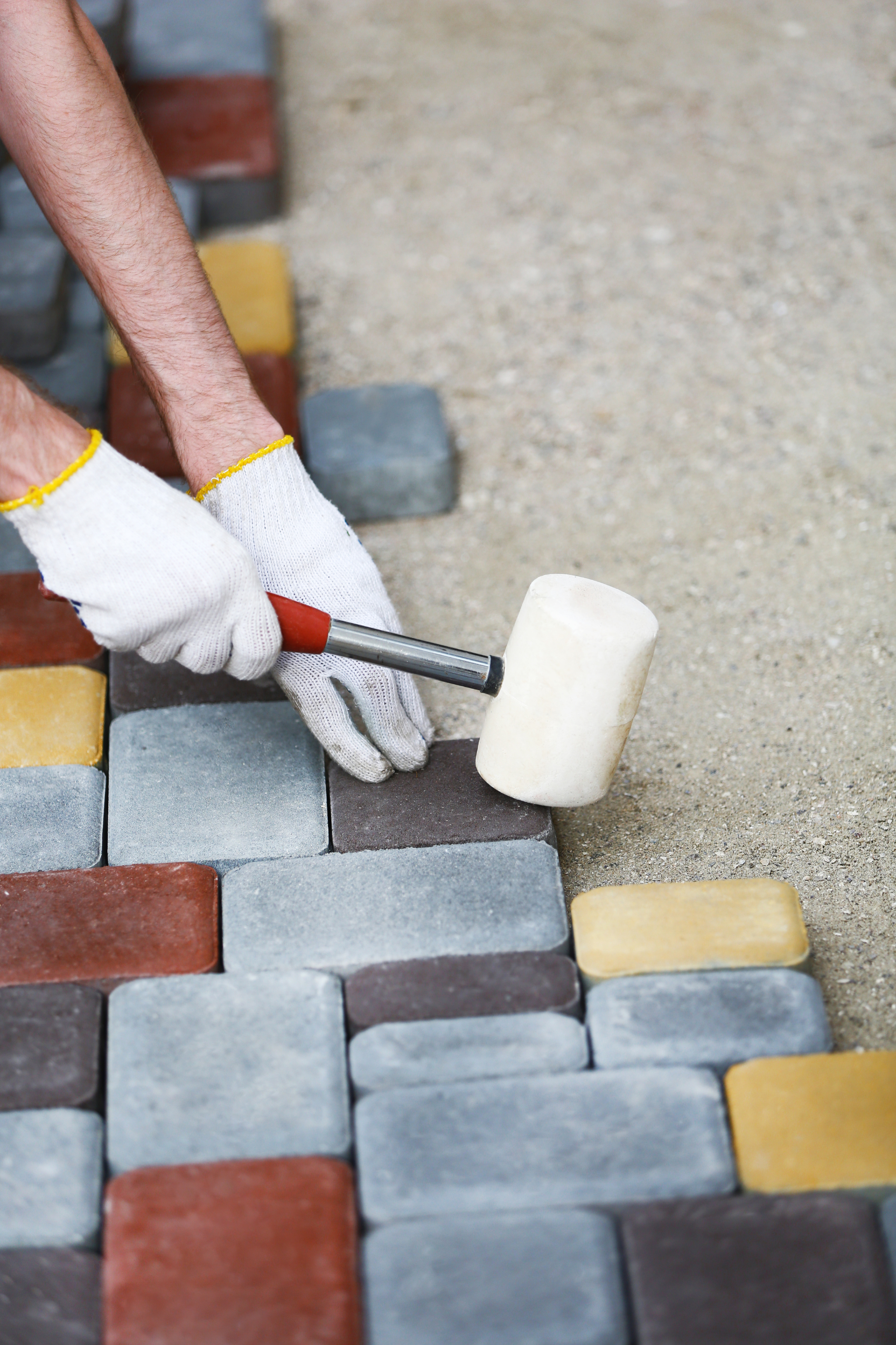 Personne posant des briques colorées avec un maillet, portant des gants de travail.