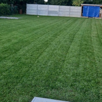 Pelouse verte avec des lignes de tonte soignées, un mur en béton et une structure.
