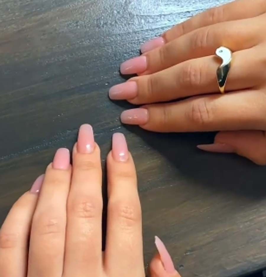 Manos de mujer con uñas rosas y un anillo de oro.