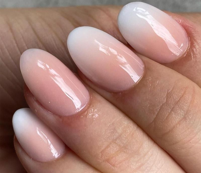 Un primer plano de las uñas de una persona con un diseño ombré rosa y blanco.