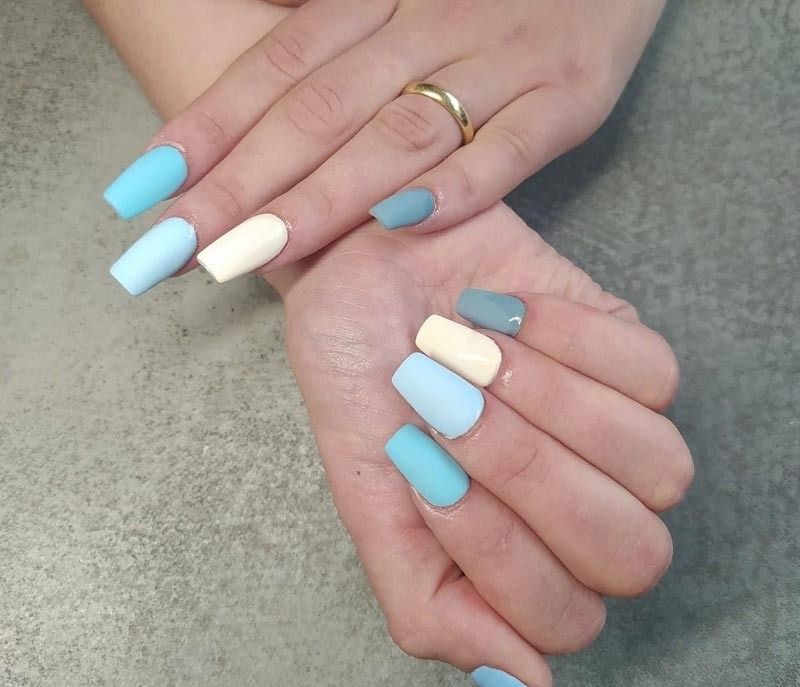 Un primer plano de las manos de una mujer con uñas azules y blancas.