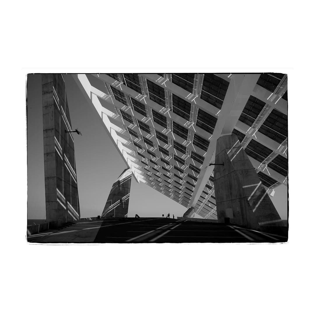 Paneles solares en un gran edificio, sostenidos por columnas, en escala de grises.