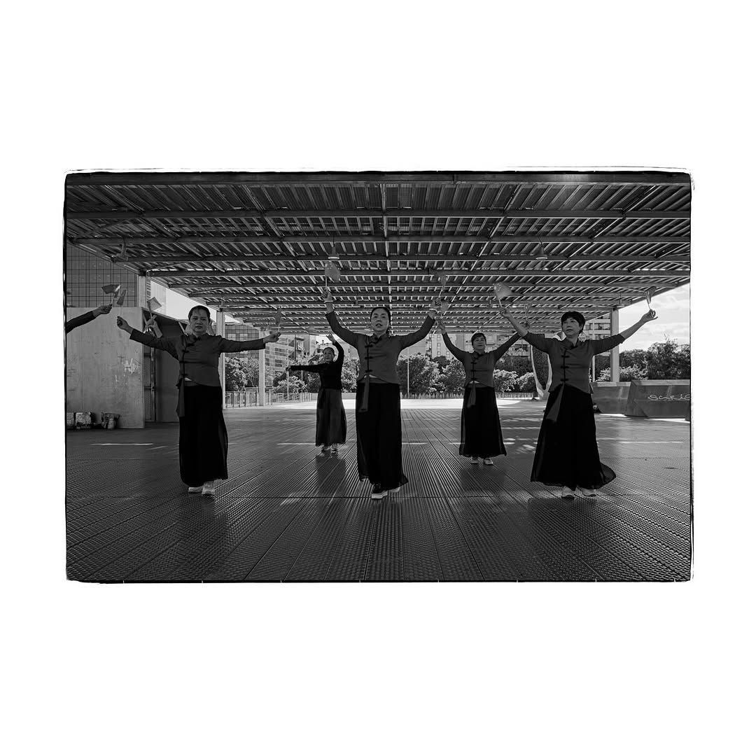 Personas con faldas largas y blusas bailan con los brazos en alto en un espacio exterior cubierto.
