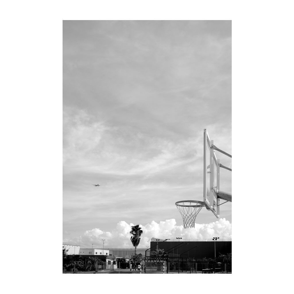 Canasta de baloncesto bajo un cielo nublado con un edificio y un árbol al fondo.