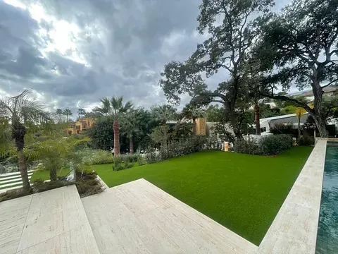 Un gran césped con una piscina al fondo y árboles al fondo.