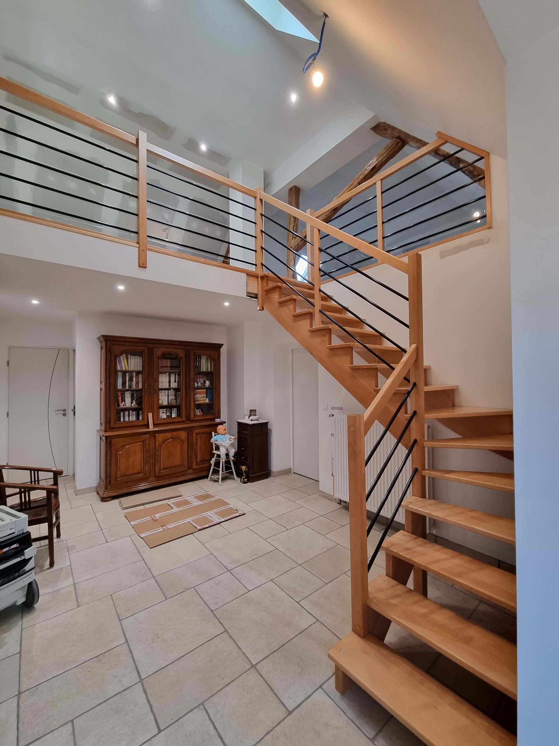 Intérieur de loft moderne avec un escalier en bois, une rampe, un sol carrelé et un meuble sous un plafond haut.