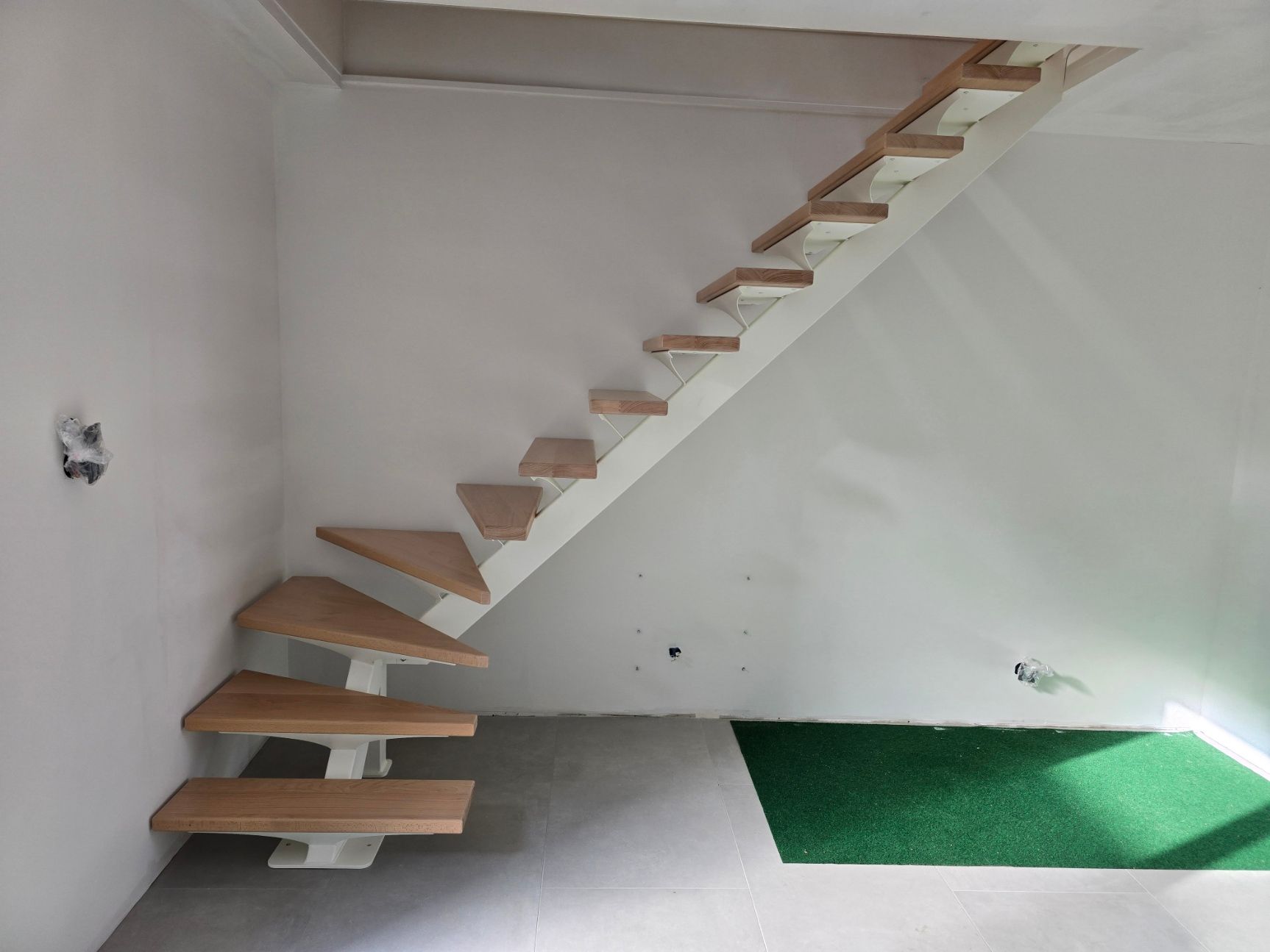 Escalier flottant en bois dans une pièce blanche avec un sol en gazon vert.