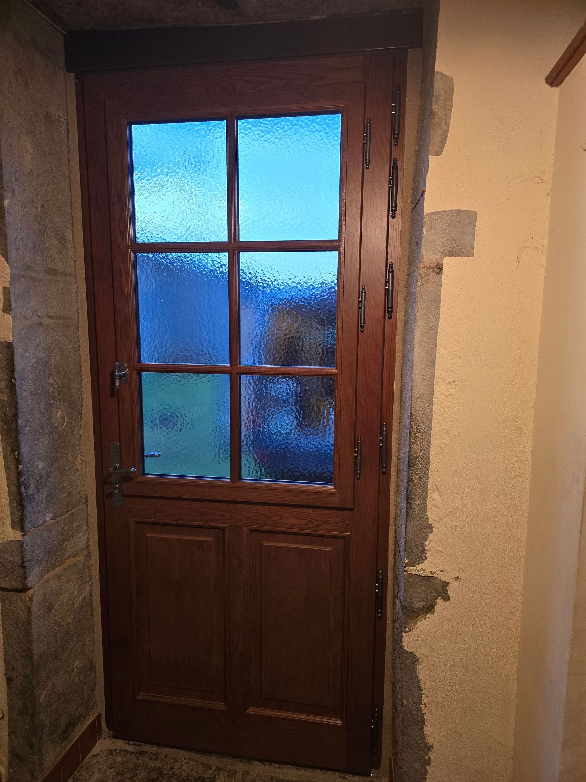 Porte en bois avec des vitres bleues dépolies dans une entrée aux murs de pierre.