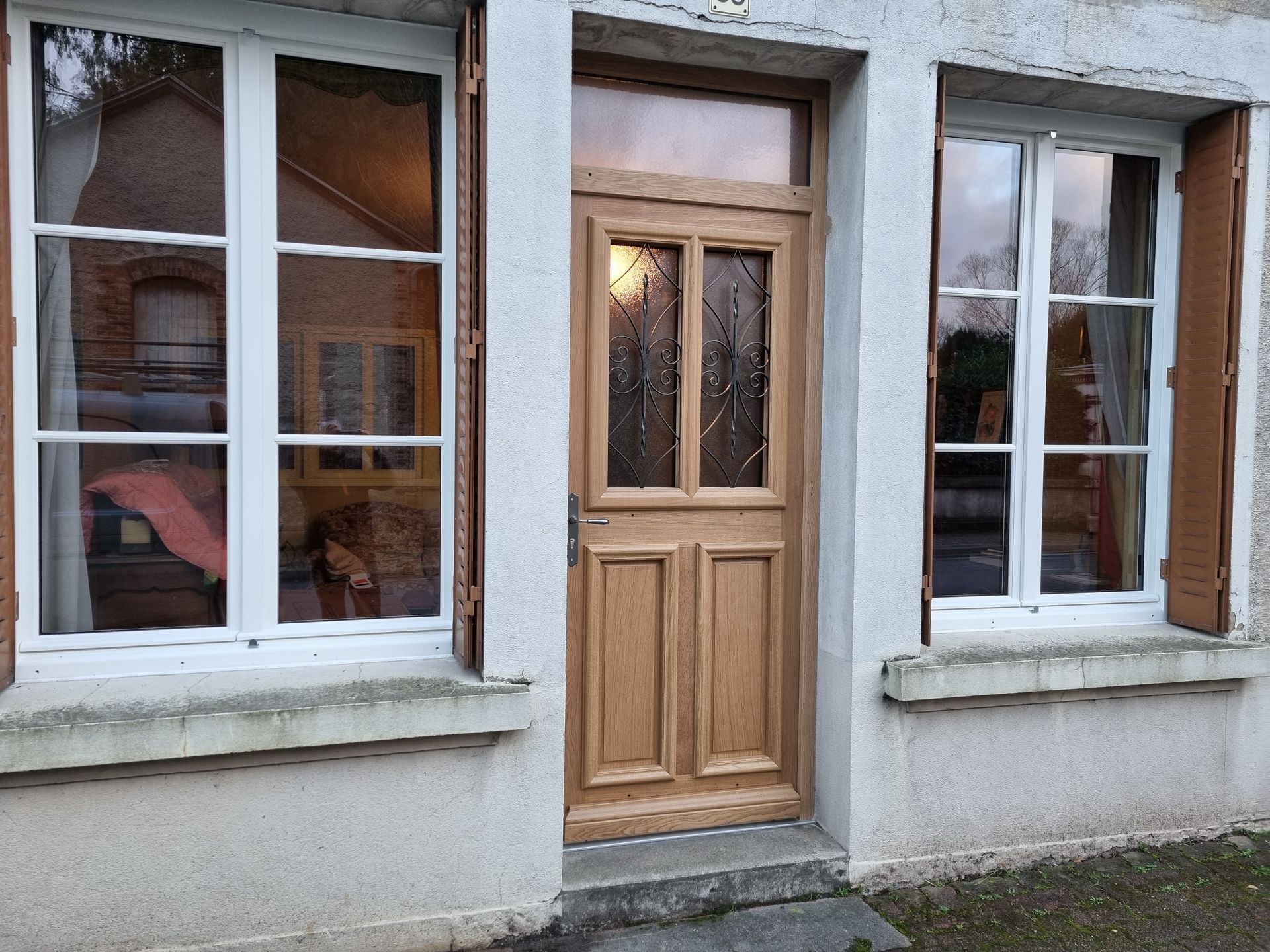 Porte d’entrée en bois entre deux fenêtres à cadre blanc sur un bâtiment en stuc gris.
