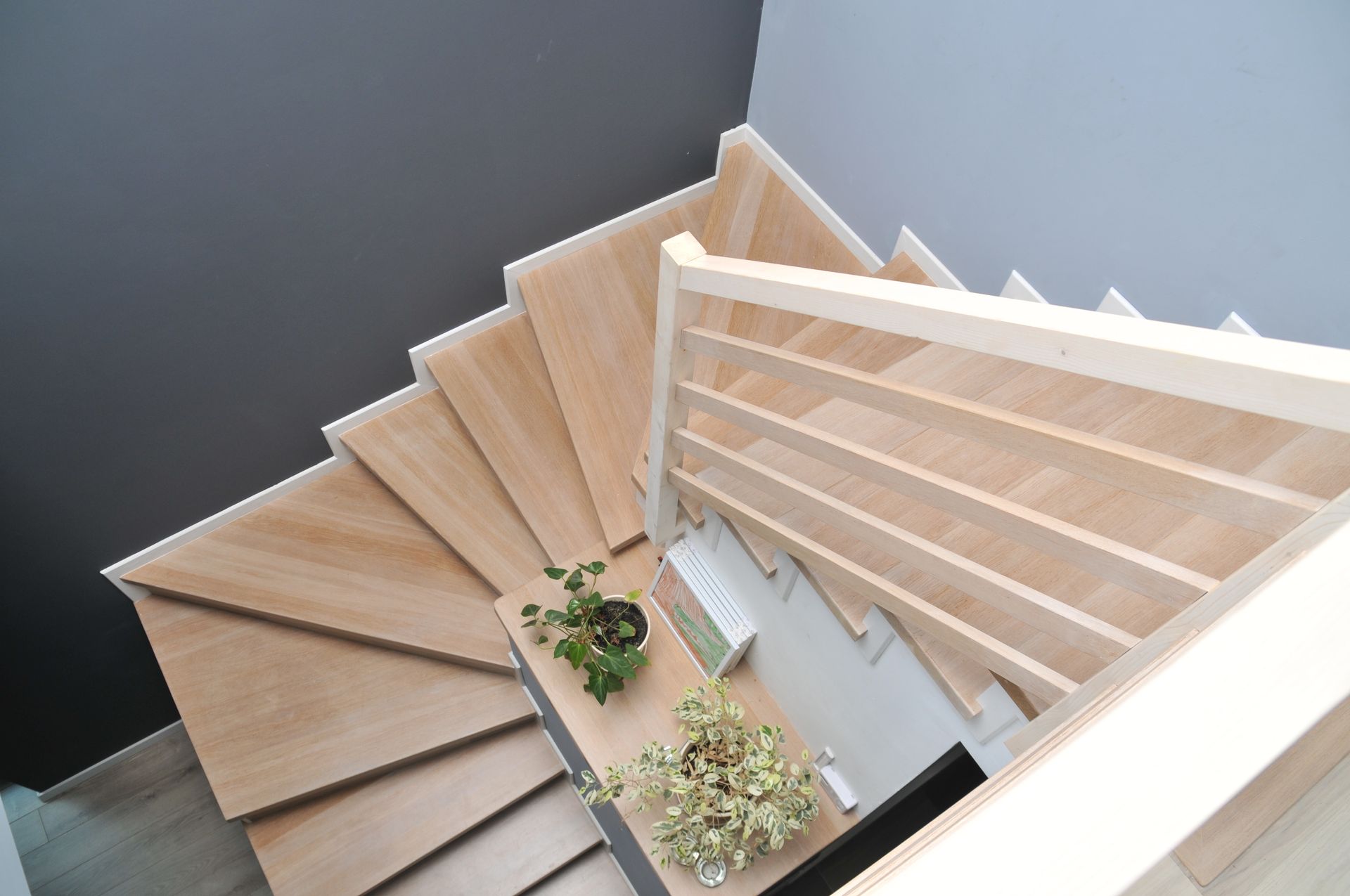 Escalier en colimaçon en bois, avec des marches claires et une petite plante en pot en dessous.