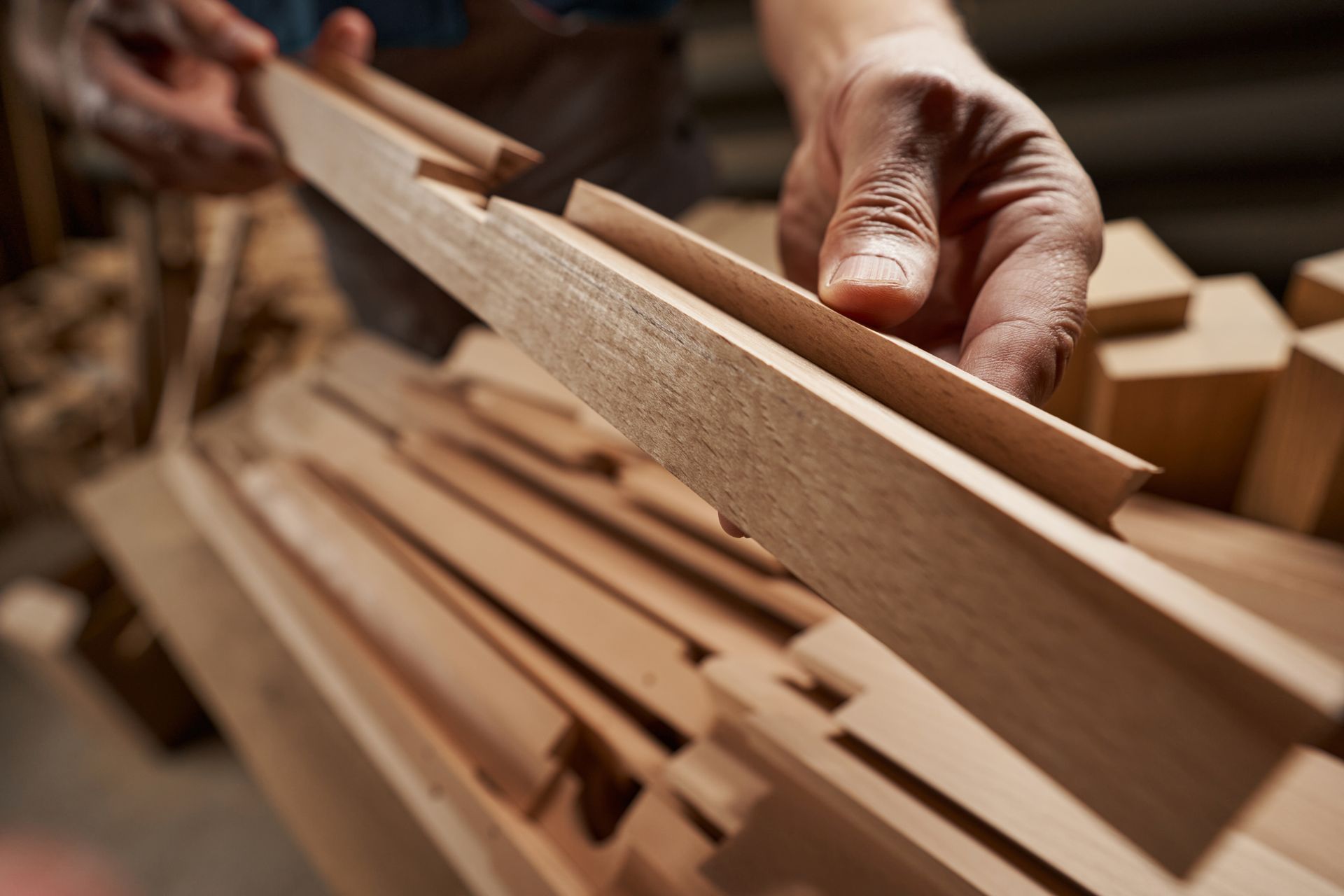 Des mains trient des planches de bois empilées dans un atelier, avec un gros plan sur des matériaux de menuiserie.