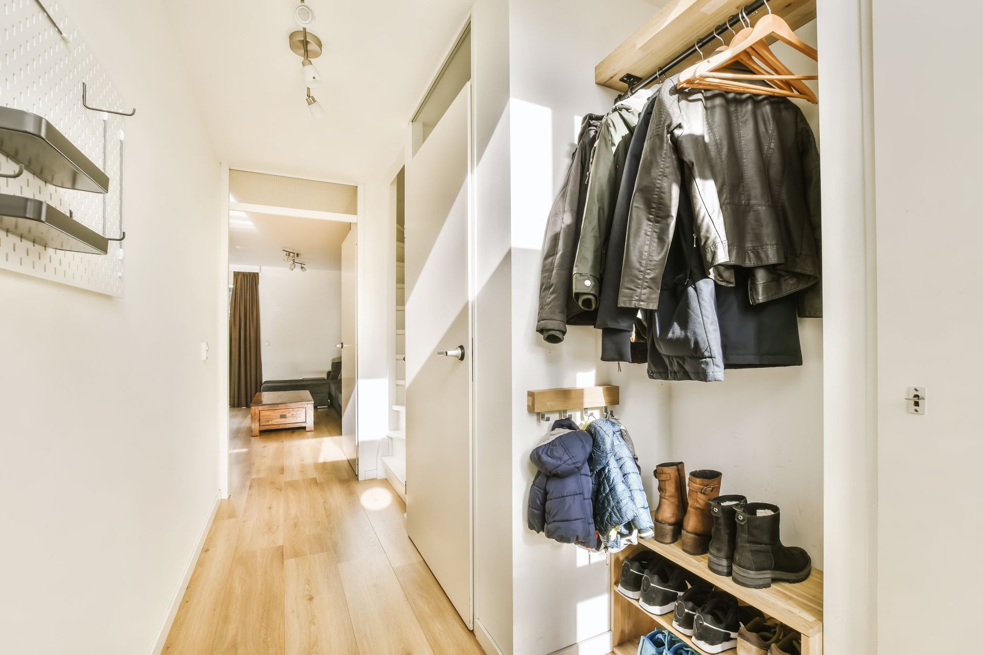 Couloir lumineux avec parquet, placard ouvert rempli de manteaux et de bottes.