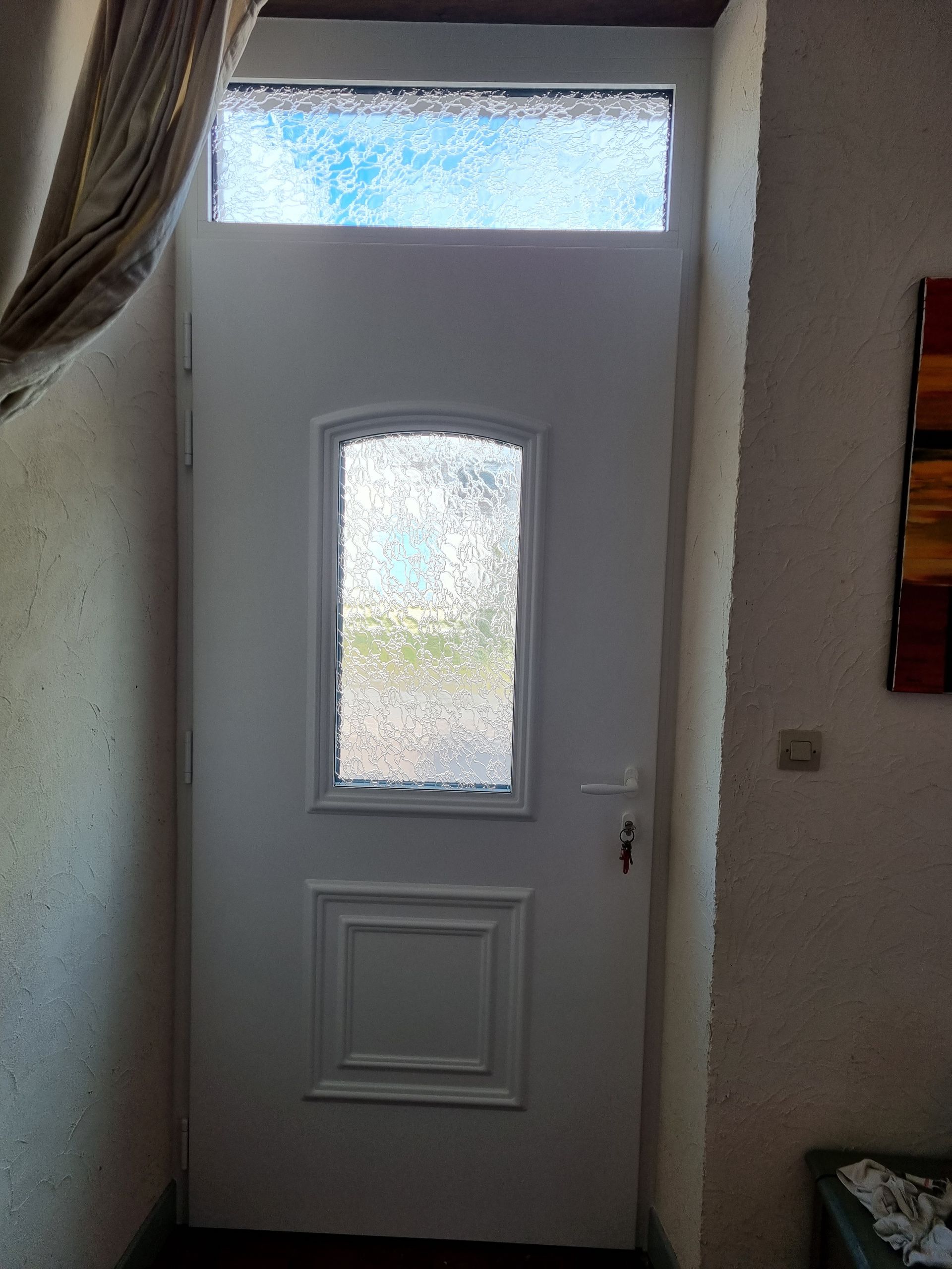 Porte d’entrée blanche avec des panneaux en verre dépoli dans un couloir étroit.