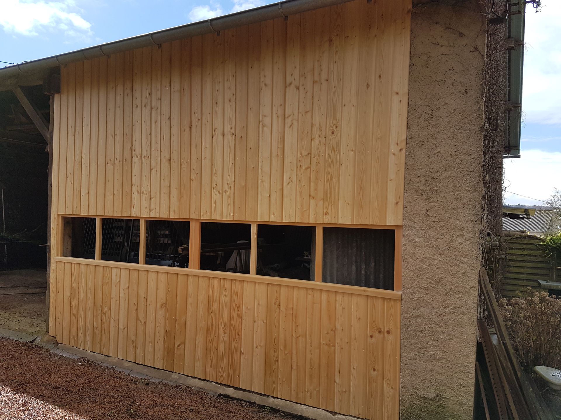 Abri de jardin en bois avec un bardage vertical et une rangée de petites fenêtres, vu de côté.