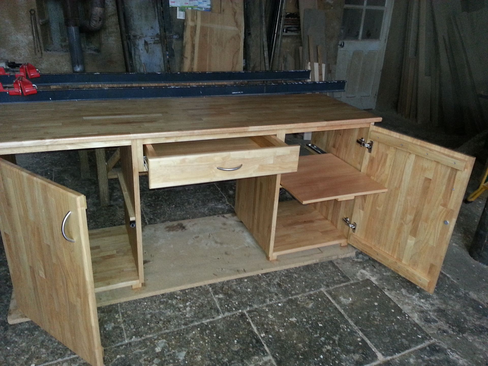 Armoire en bois aux portes et tiroirs ouverts, dans un atelier, laissant voir des étagères non finies et des compartiments de rangement.