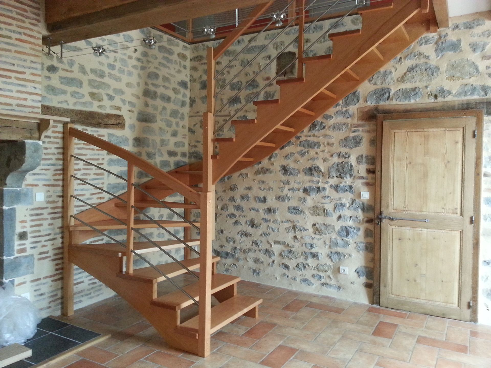 Intérieur rustique avec des murs en pierre, un sol carrelé et un escalier en bois menant à l’étage.