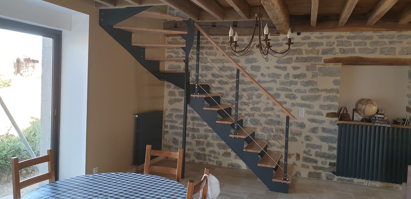 Escalier avec une rampe noire le long d’un mur en pierre dans une salle à manger rustique.