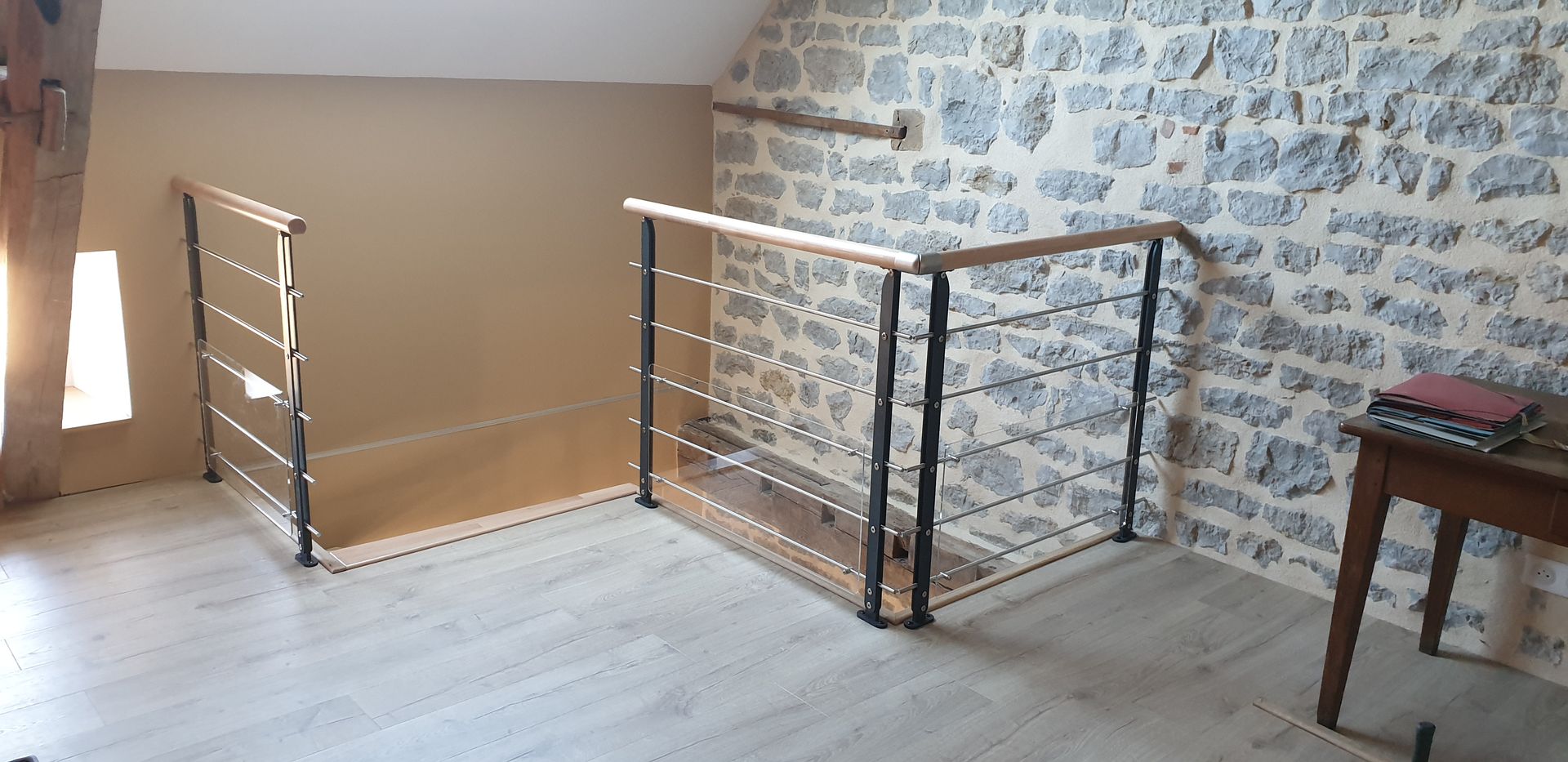 Palier de mezzanine vide avec un mur en pierre, un plancher en bois et une rambarde en métal noir près d’une fenêtre.