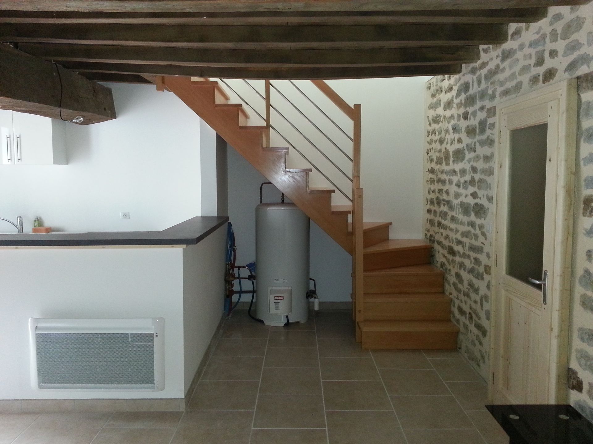Intérieur rustique de sous-sol avec un escalier en bois, un mur en pierre, un sol carrelé et un chauffe-eau.