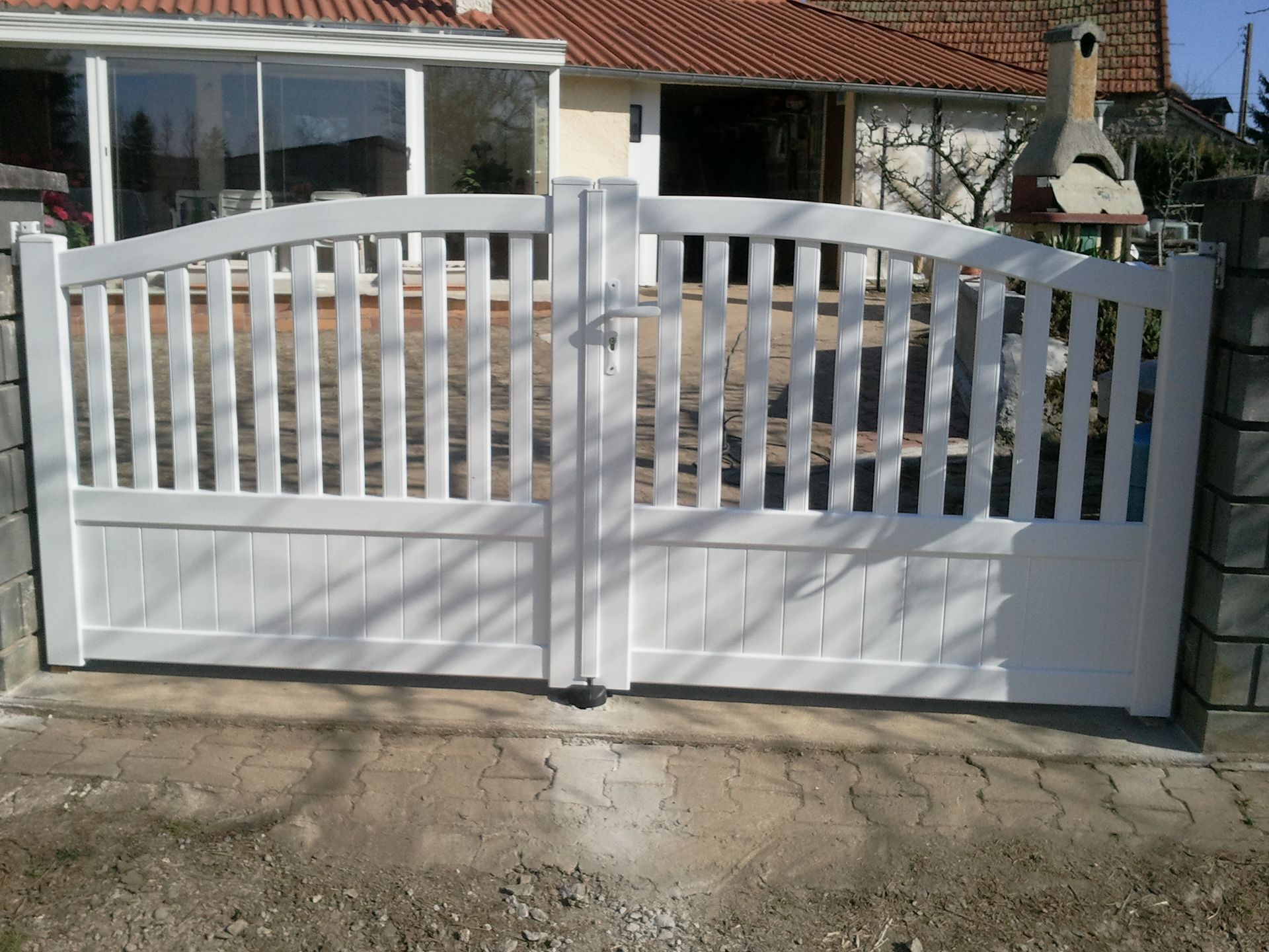 Portail d’entrée blanc en bois devant une maison et une terrasse.