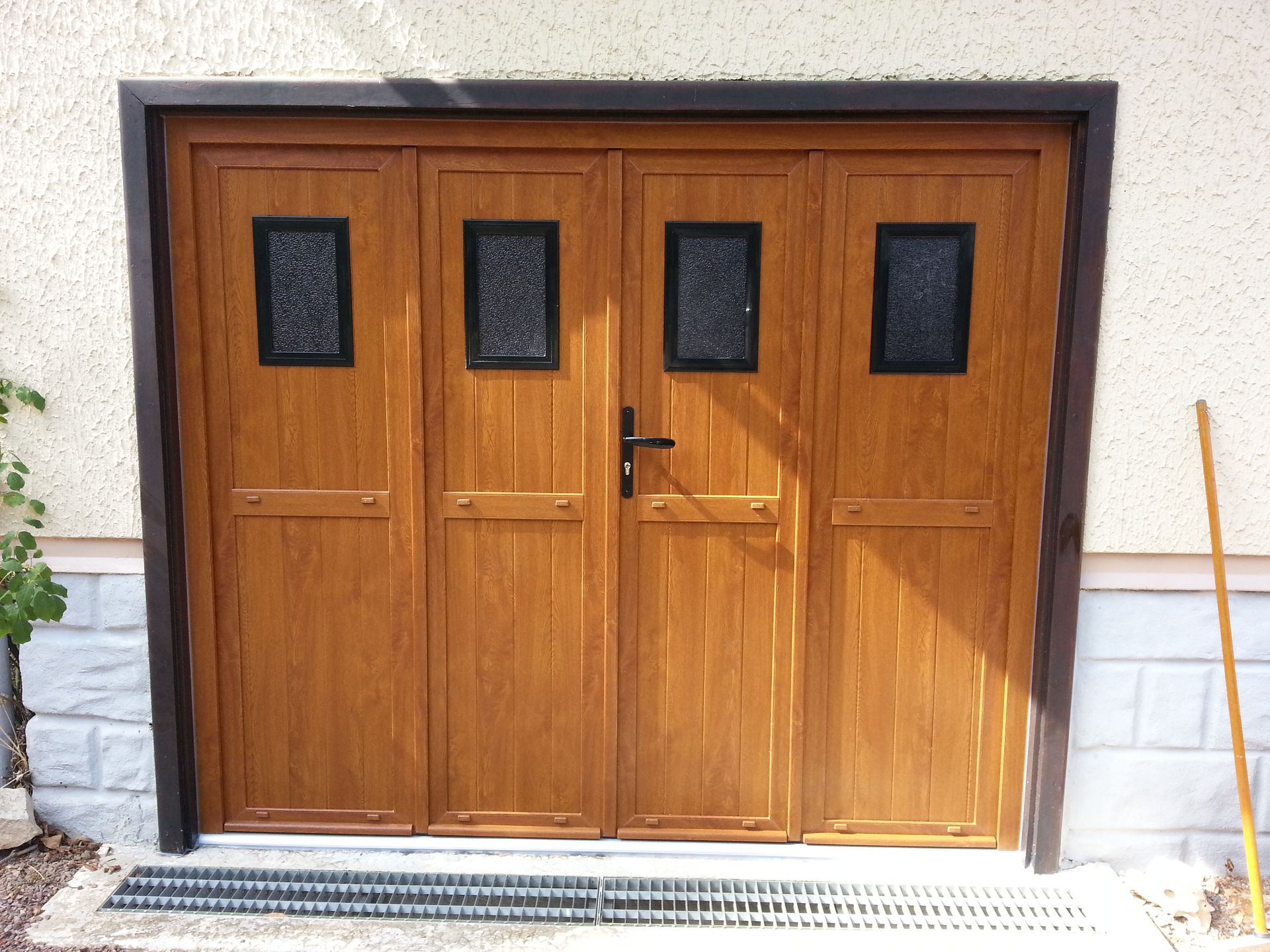 Portes en bois de style garage, à quatre panneaux et ornées de petites fenêtres, dans un mur en stuc.