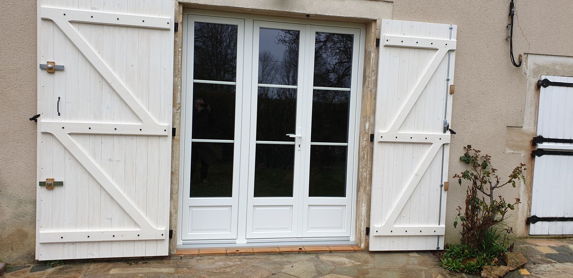 Portes-fenêtres blanches avec volets sur la façade beige d’une maison.