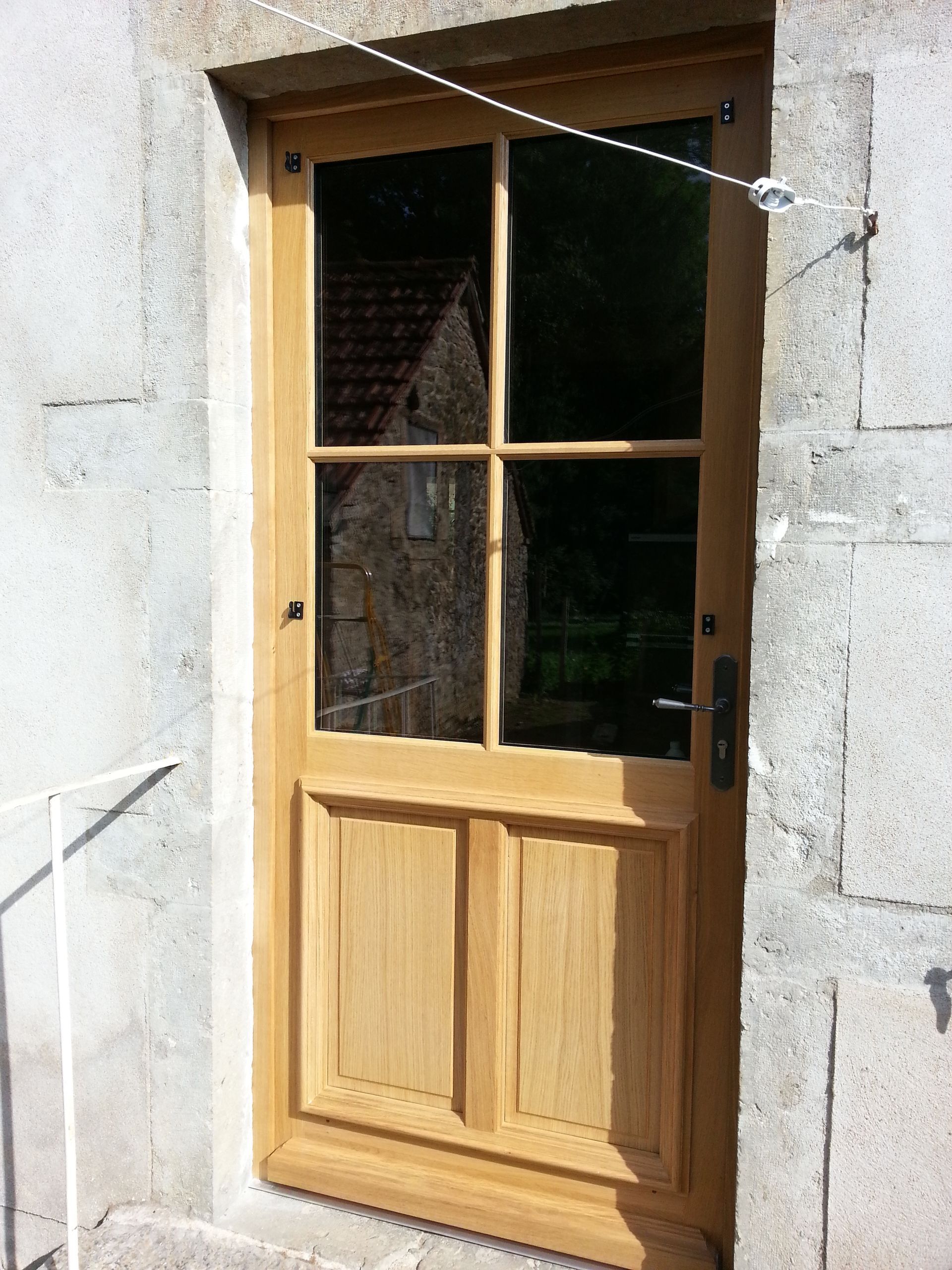 Porte en bois à panneaux vitrés encastrée dans un mur en pierre, avec un loquet métallique à droite.