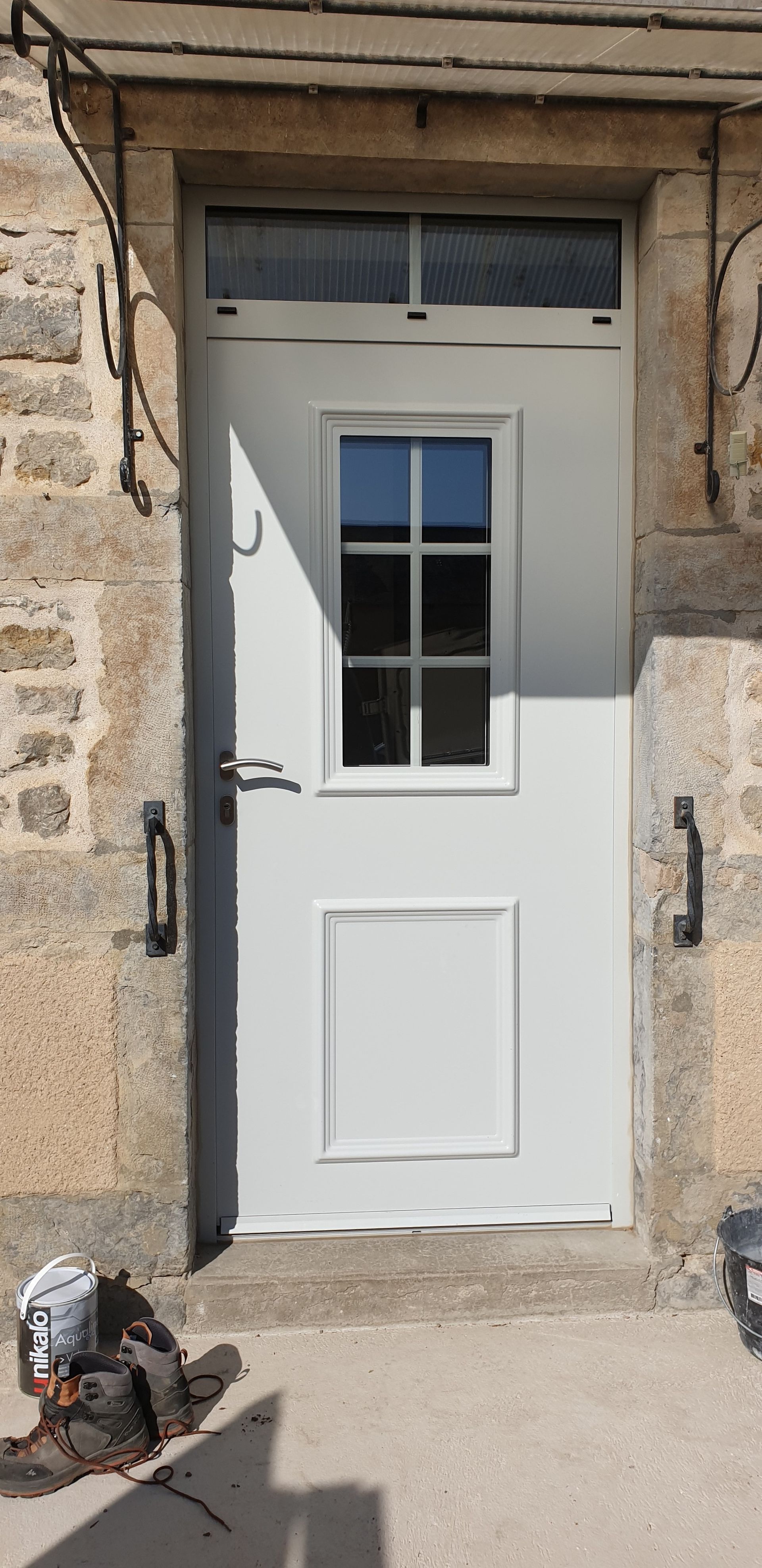 Porte blanche dans un mur de pierre, avec une petite fenêtre et un câble emmêlé au sol.