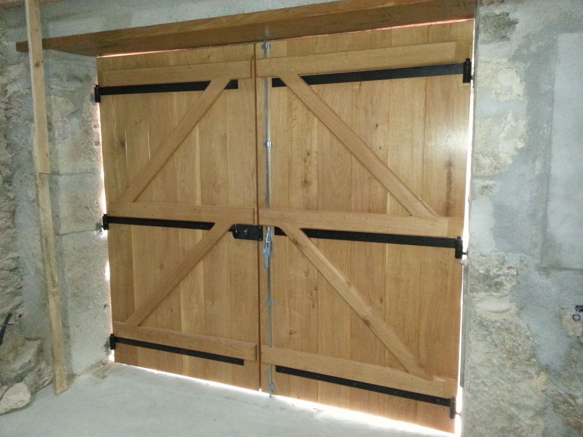 Portes doubles en bois de style grange, avec des renforts diagonaux et une quincaillerie en métal noir.