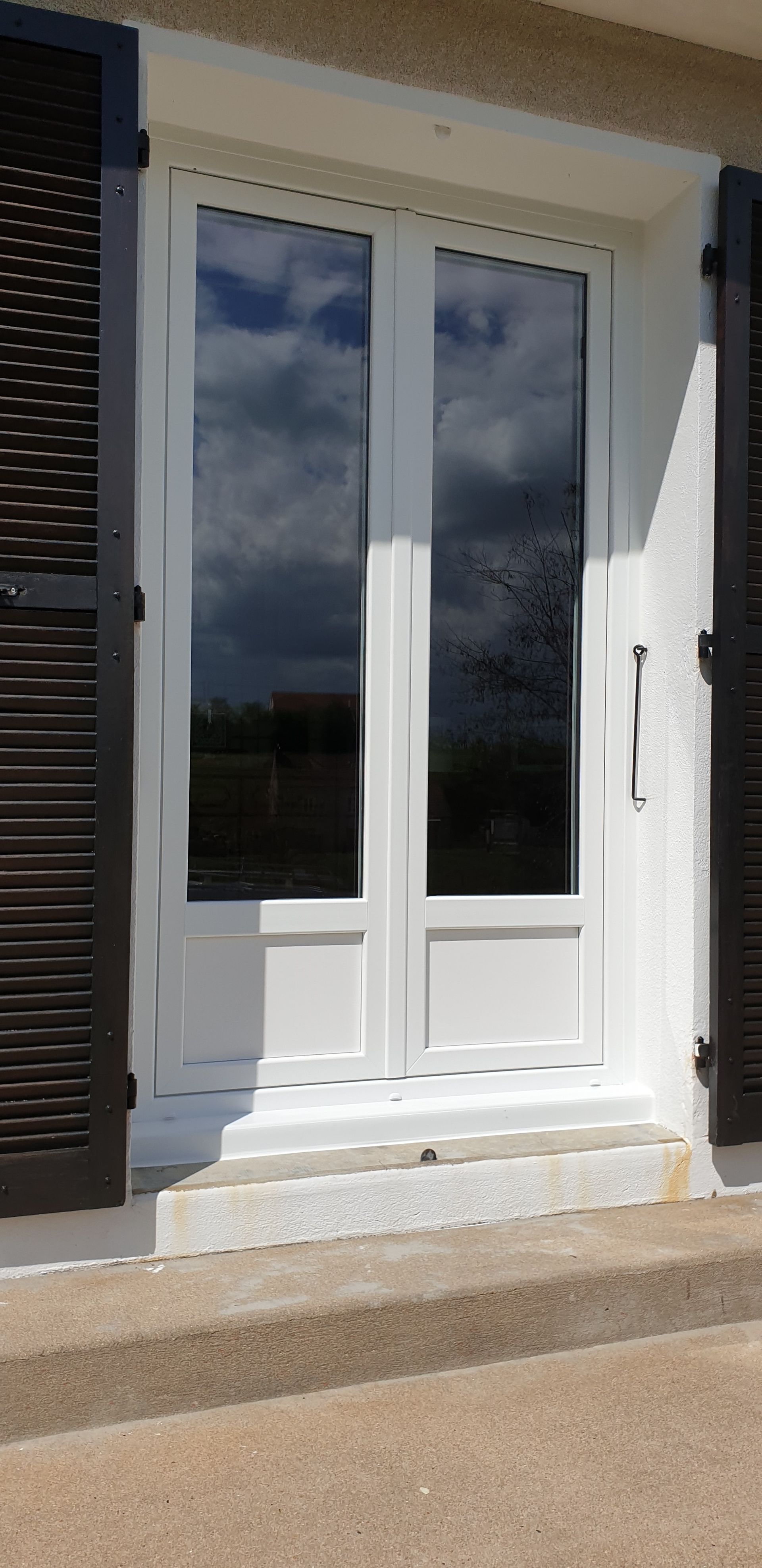 Porte d’entrée double blanche avec des panneaux vitrés et une petite marche devant la maison.