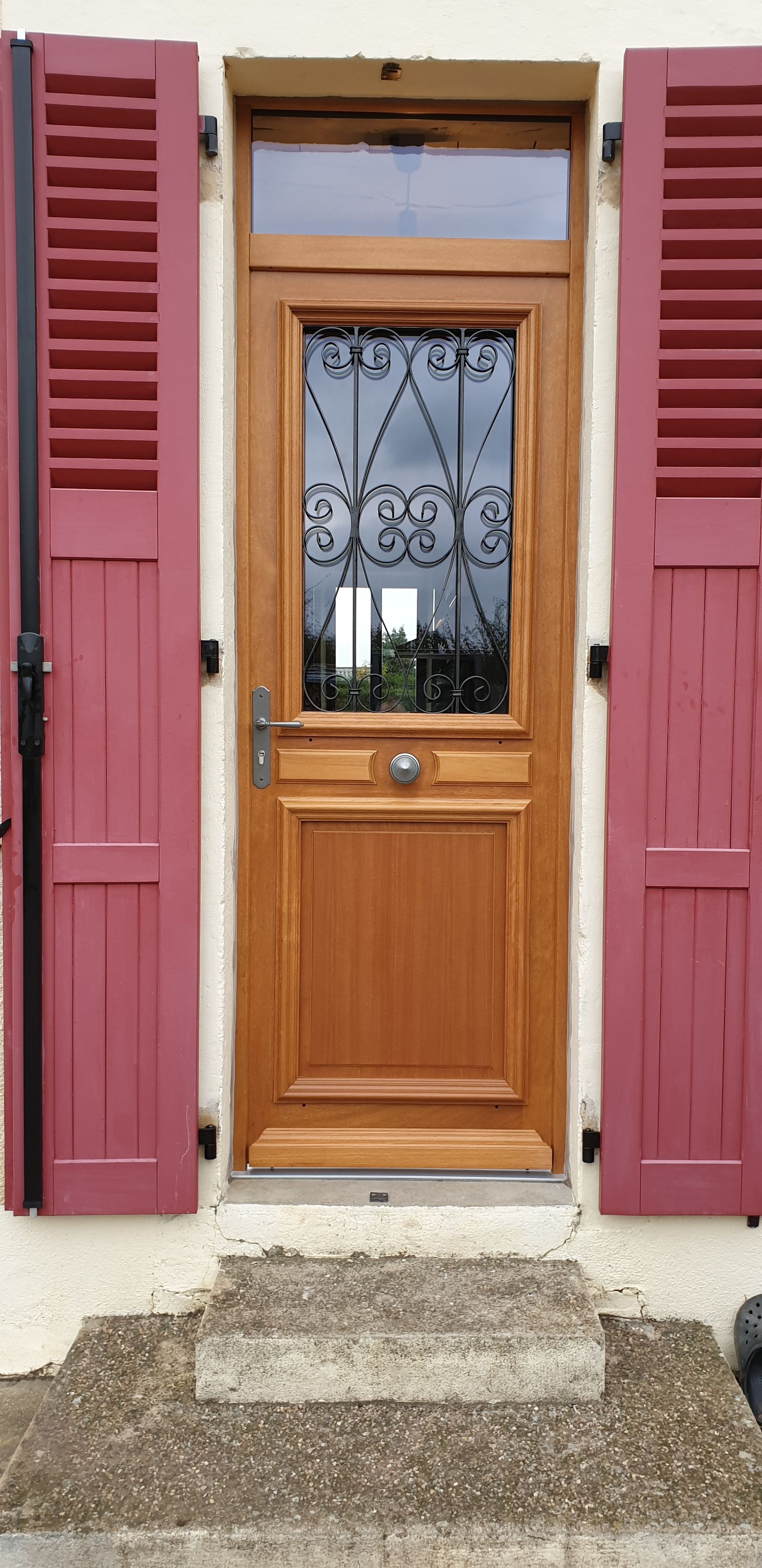 Porte d’entrée en bois avec des volets rouges et une petite marche en béton devant.