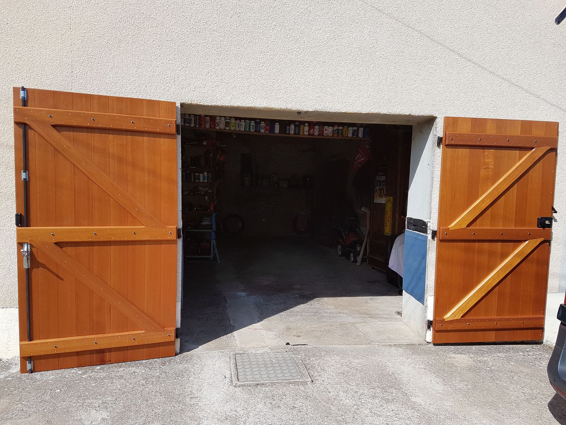 Ouvrez les doubles portes en bois donnant sur l’intérieur sombre d’un garage, avec un mur extérieur blanc.