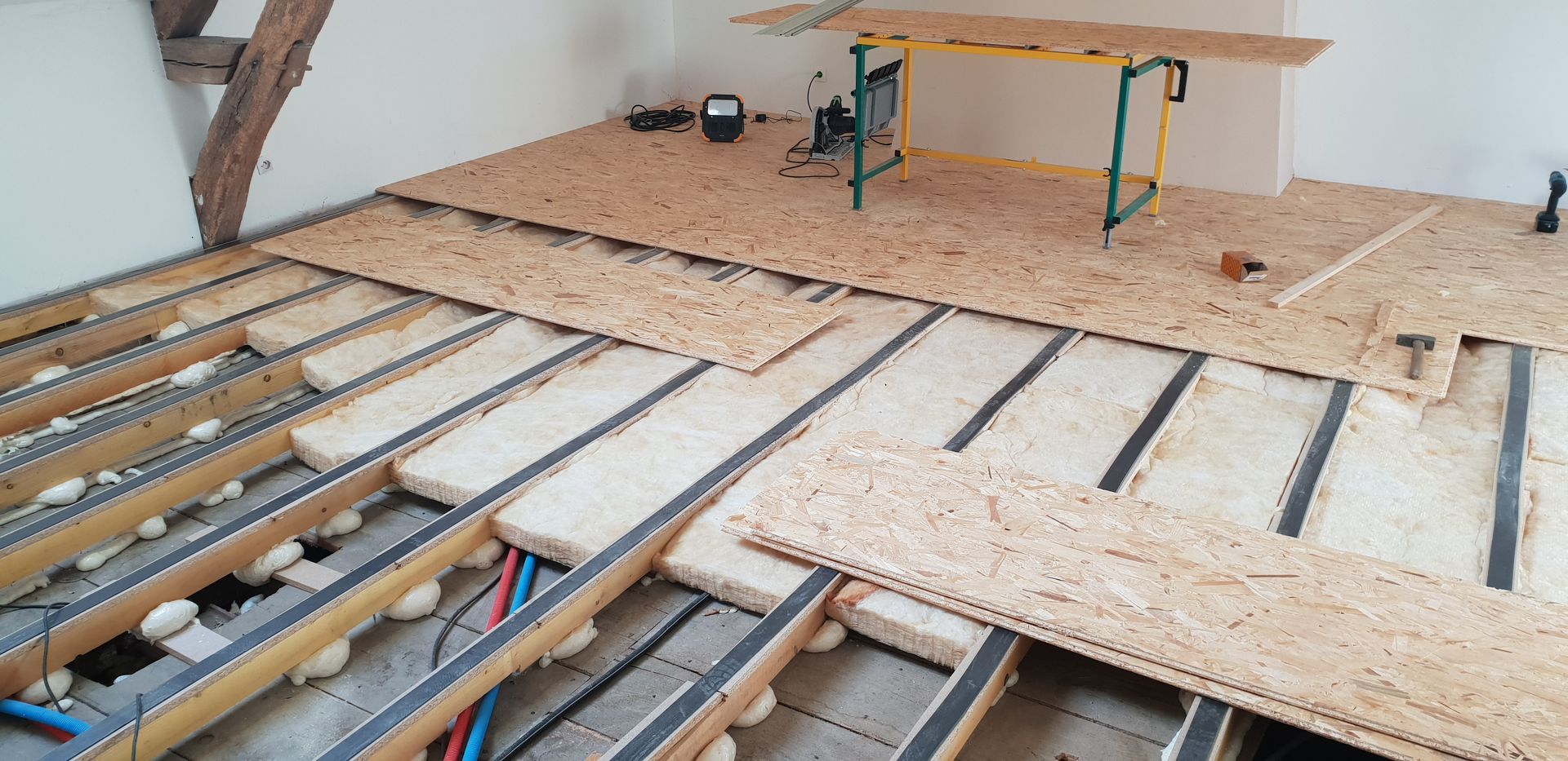 Plancher partiellement construit, avec solives apparentes et panneaux de contreplaqué dans un atelier.