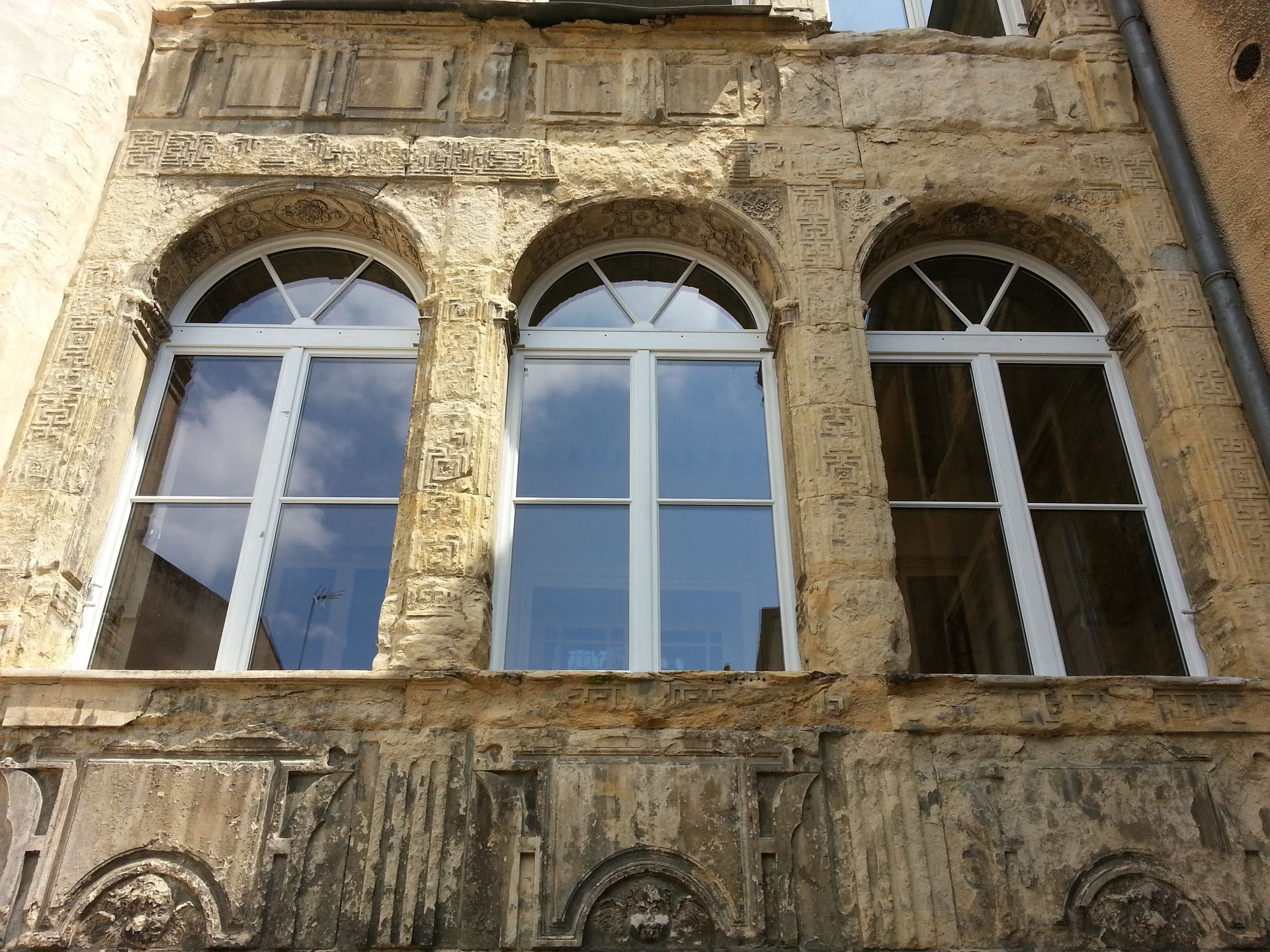 Façade d’un ancien bâtiment en pierre, avec trois fenêtres cintrées et des détails ouvragés patinés par le temps.