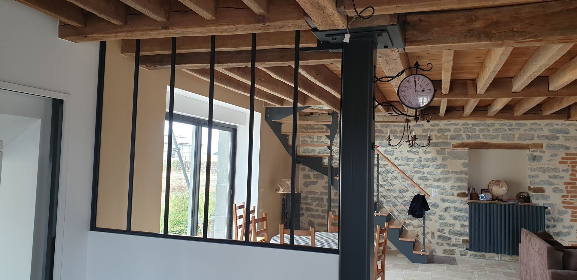 Intérieur de loft moderne avec poutres apparentes, claustra noir, mur en pierre et une personne près de la cheminée.