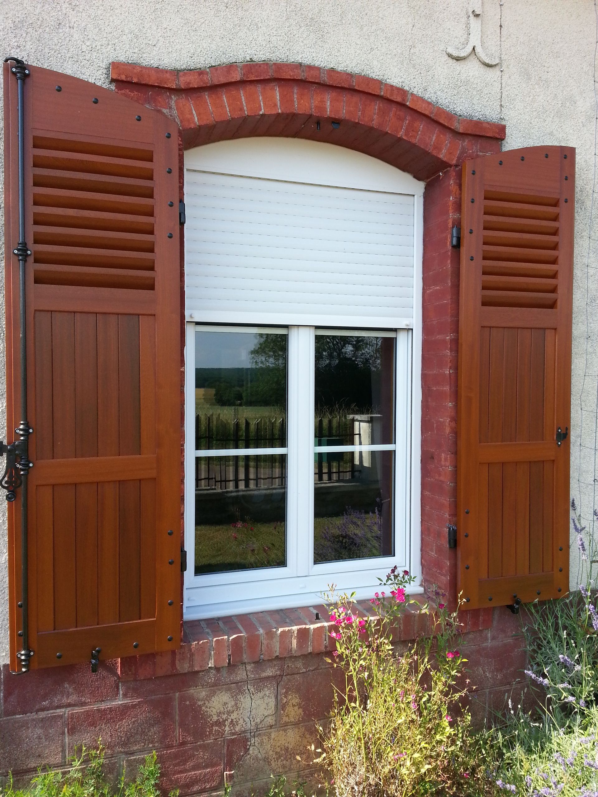 Fenêtre blanche avec une arche en briques rouges et des volets bruns.