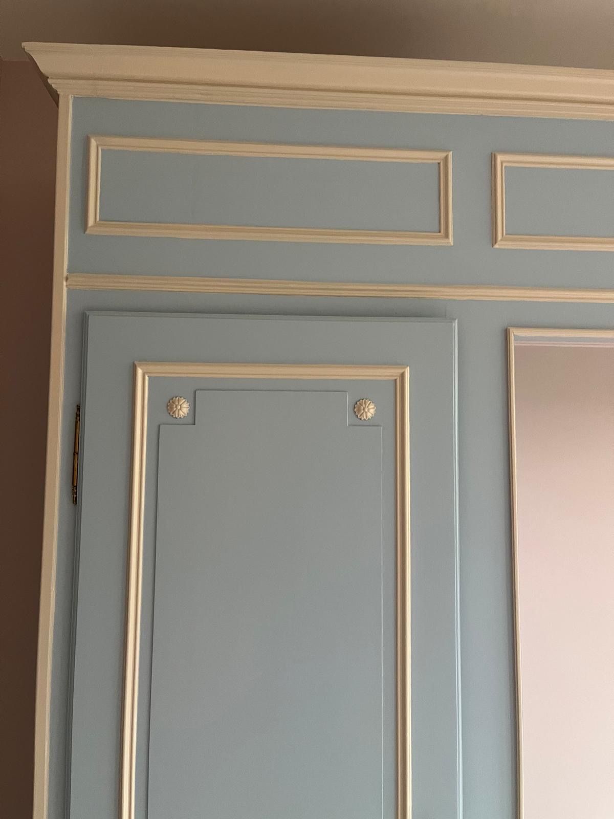 Une armoire bleu clair ornée de garnitures, de moulures et de petits motifs floraux blancs.