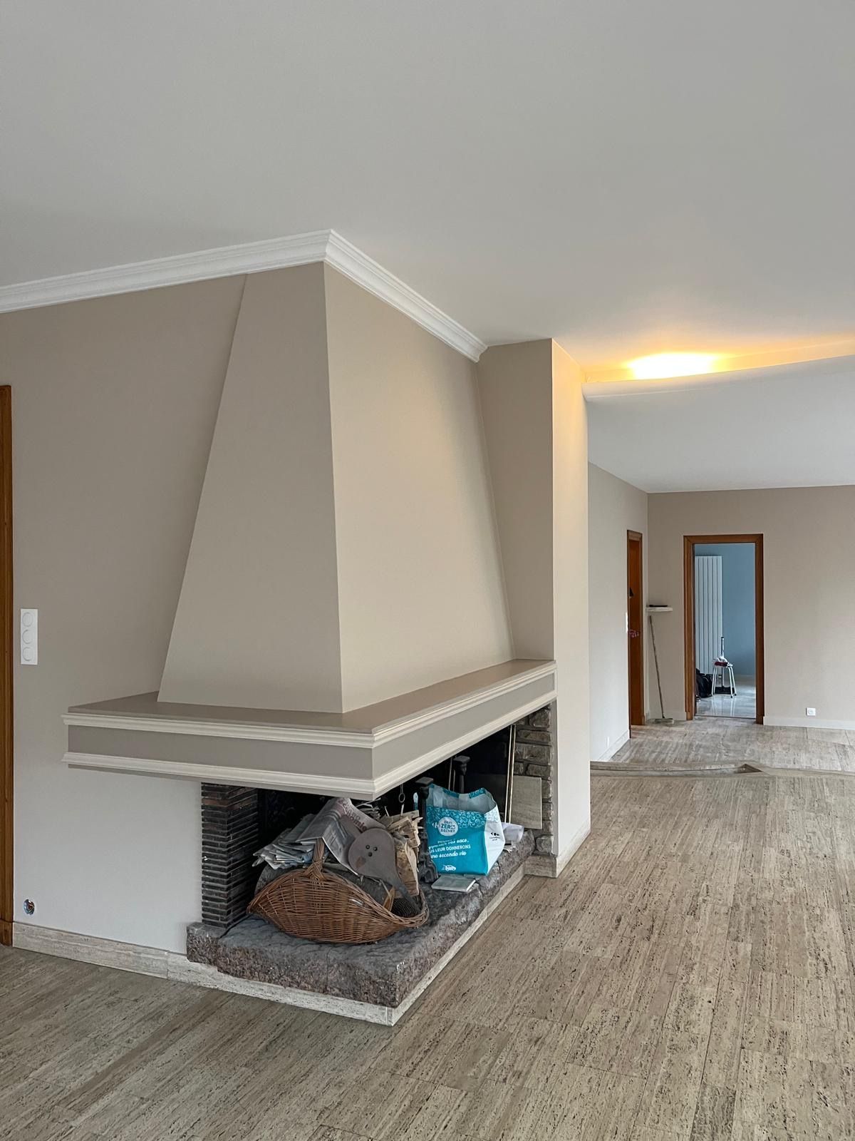 Une cheminée beige avec un foyer en pierre et une hotte inclinée, située dans une pièce au sol clair.