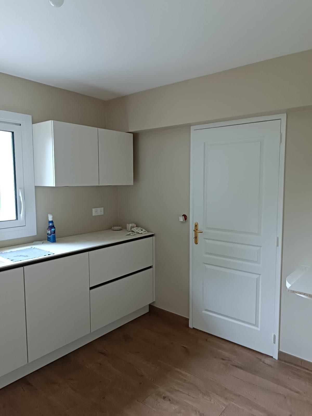 Coin cuisine moderne avec placards blancs, plan de travail, sol imitation bois et porte intérieure blanche.