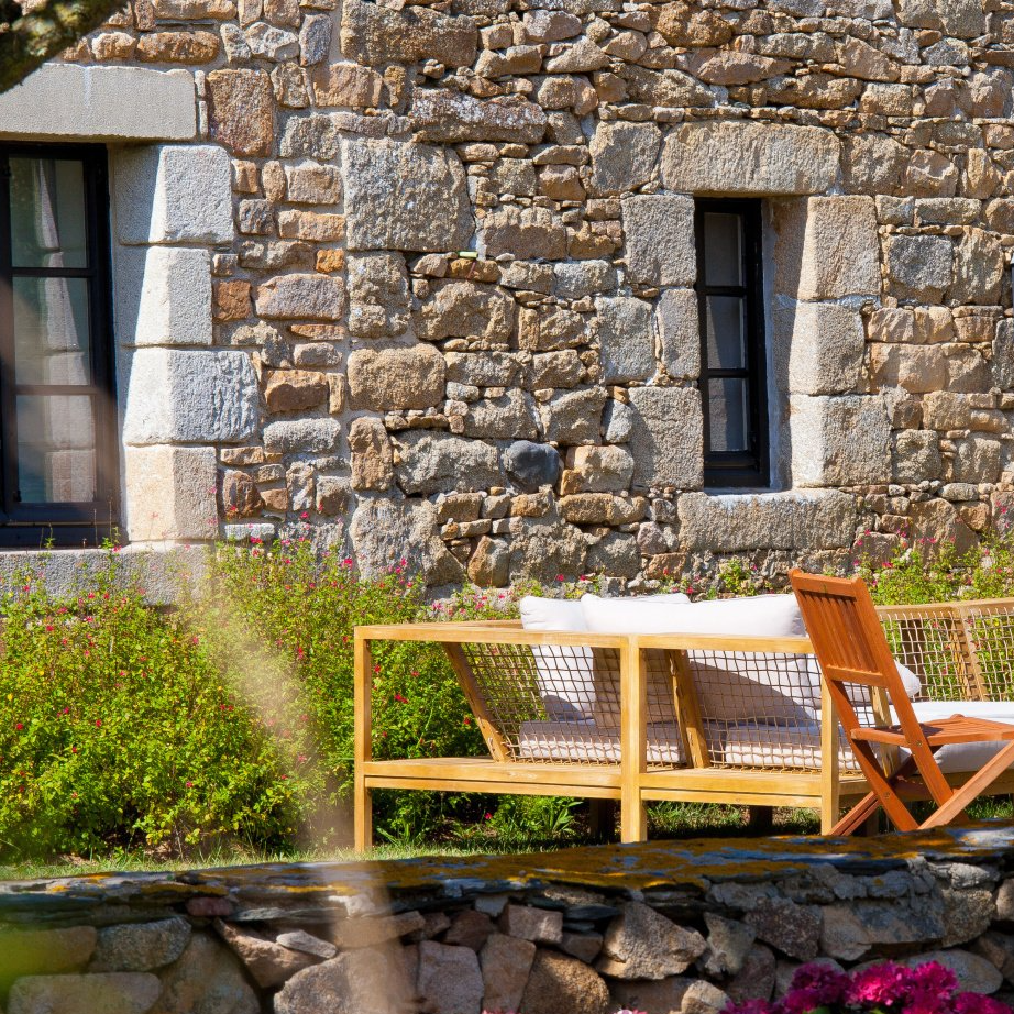 Une façade en pierre ancienne rénovée et des meubles de terrasse en bois
