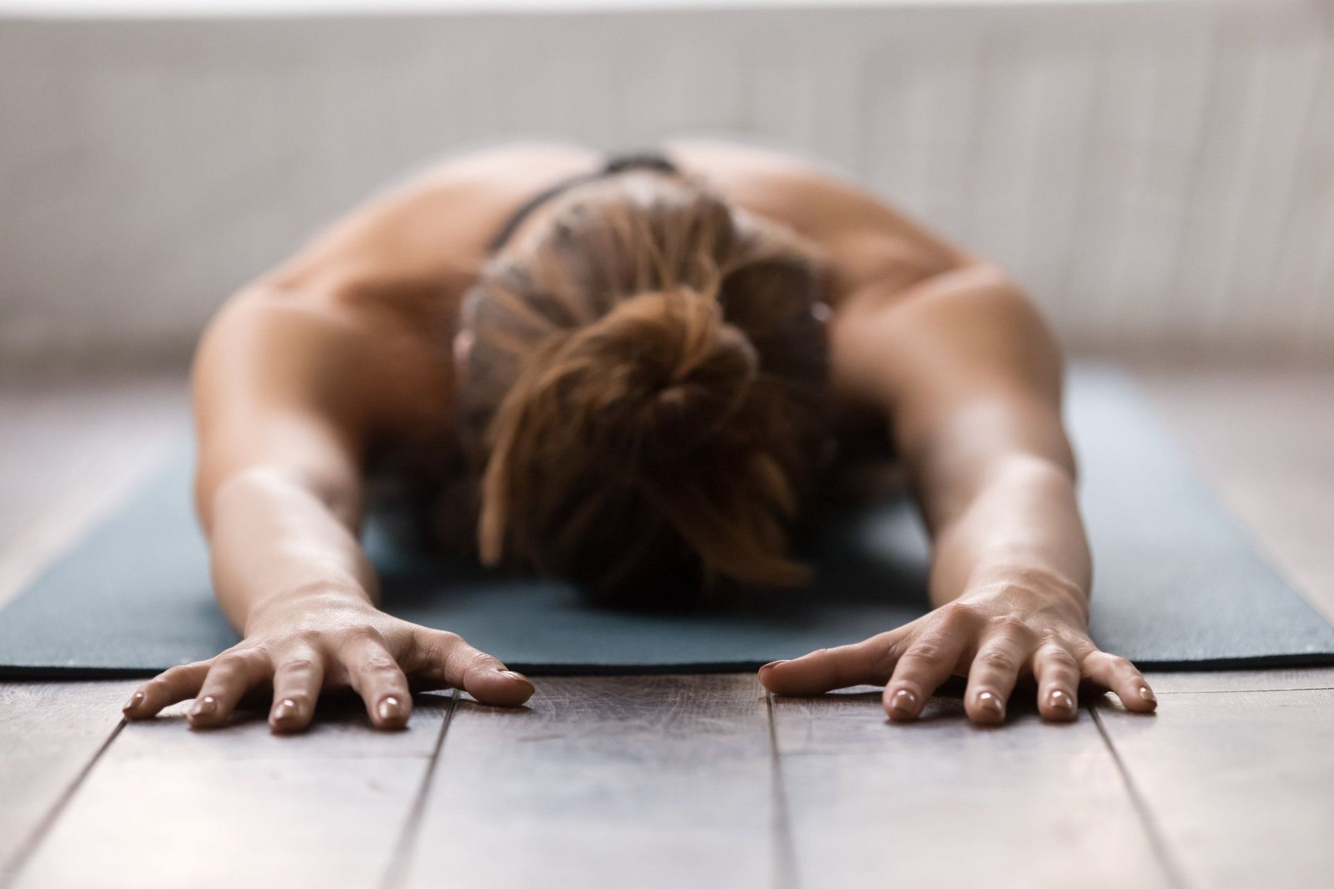 Una mujer está tumbada sobre una esterilla de yoga con la cabeza agachada.