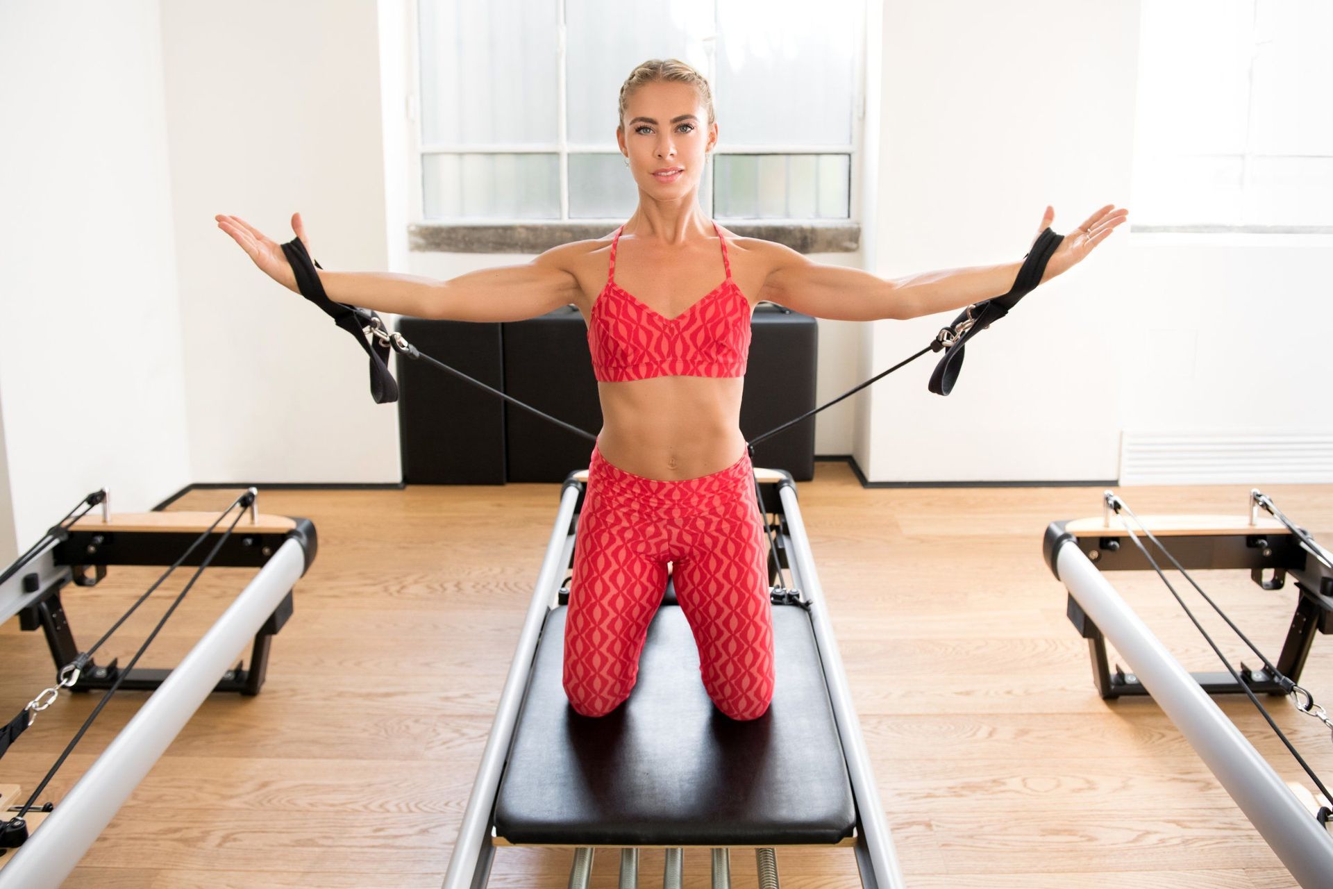 Una mujer está arrodillada en una máquina de pilates con los brazos extendidos.