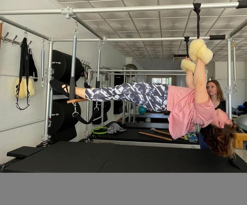 Una mujer con una camisa rosa está boca abajo en una máquina de pilates.