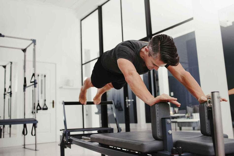 Un hombre está haciendo flexiones en una máquina de pilates en un gimnasio.