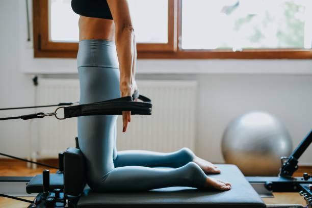 Una mujer está arrodillada en una máquina de pilates en un gimnasio.